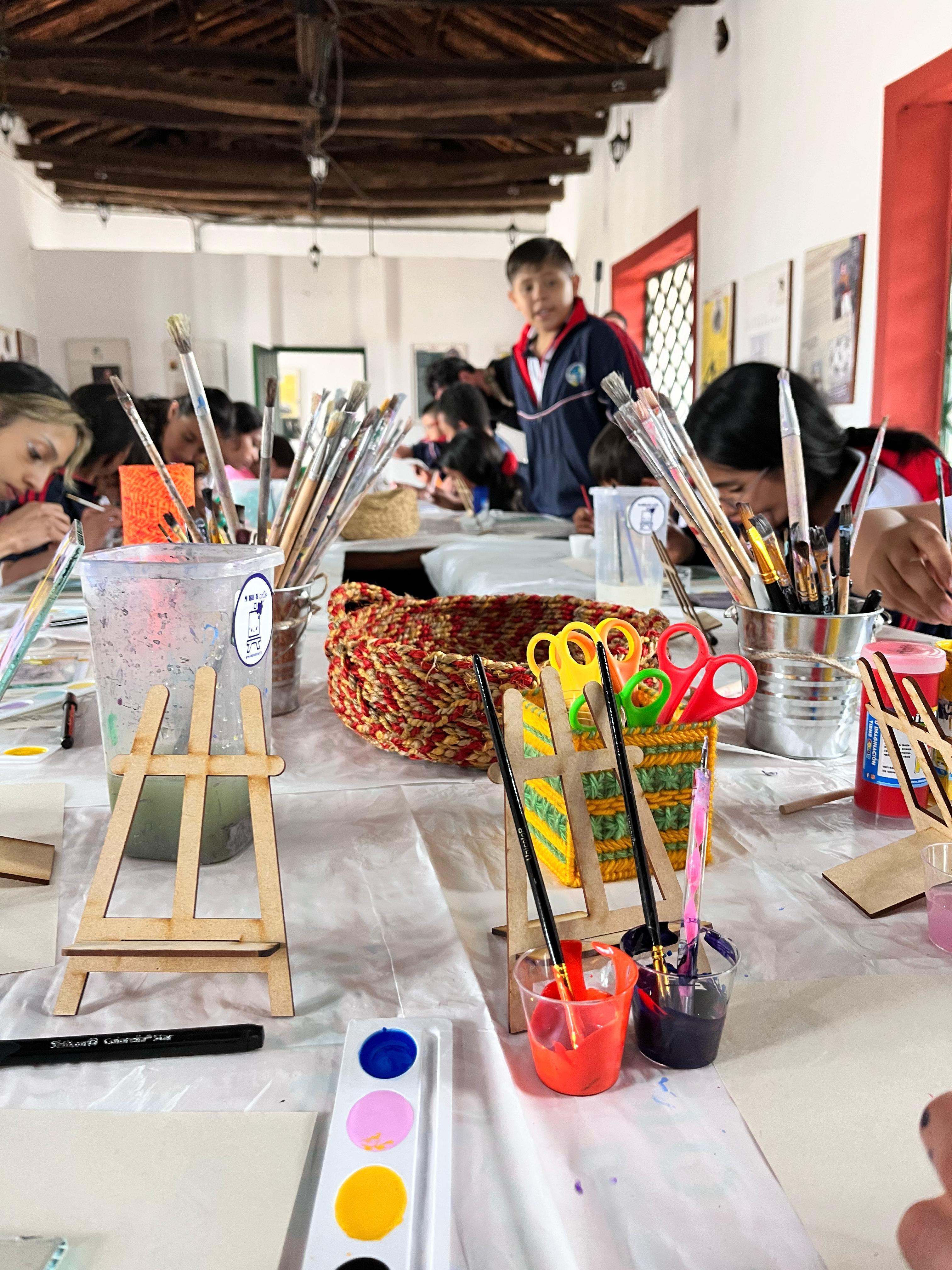 Materiales de arte sobre una mesa. Ni&ntilde;os al fondo.